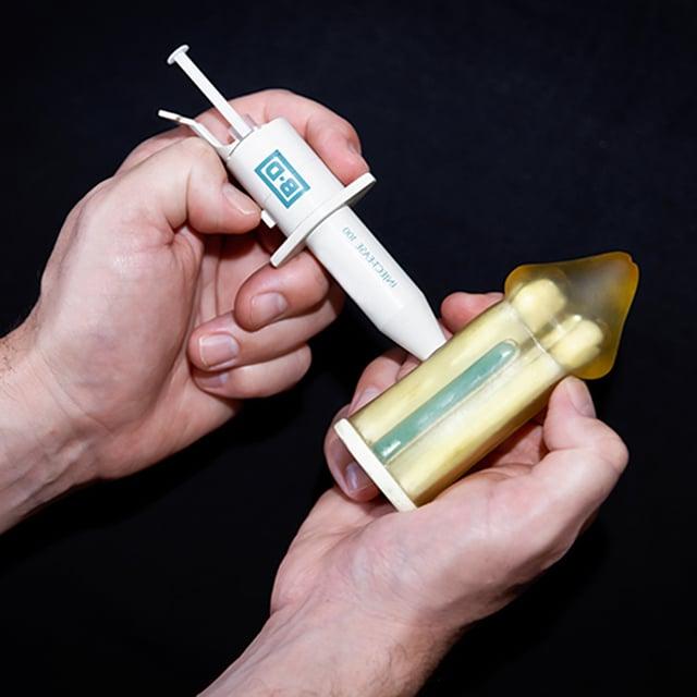 Demonstration of an auto injector positioned perpendicular and halfway down the shaft, highlighting the spring-loaded button. 